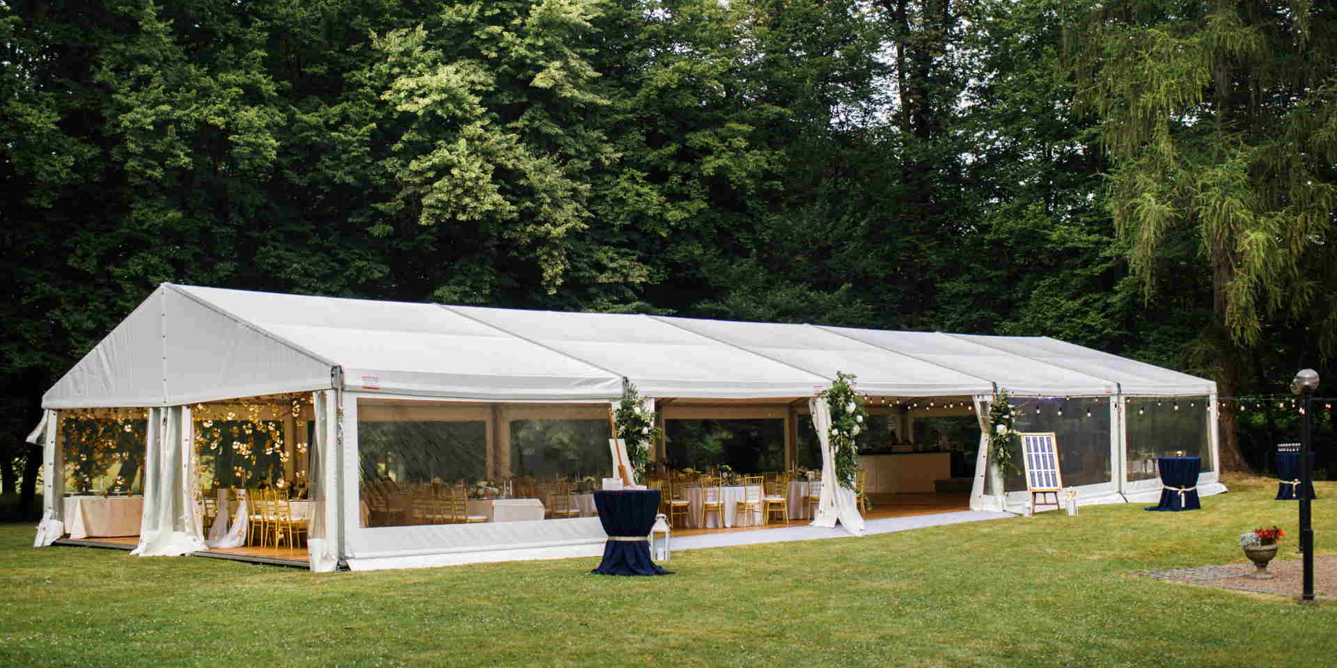 Long white tent for wedding party in the woods.